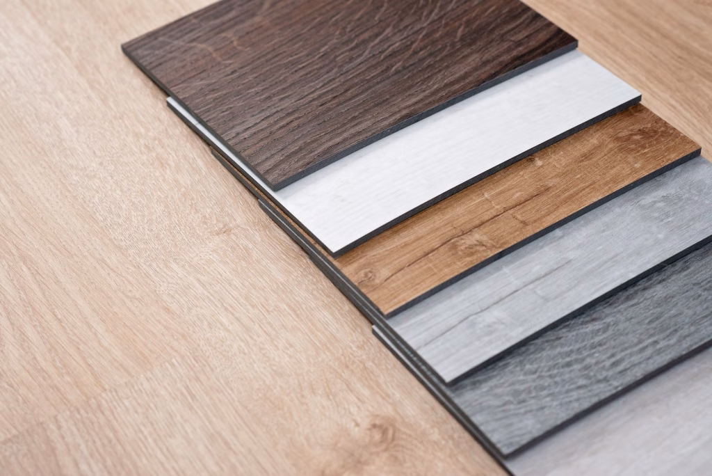 Floor covering samples in timber-look and grey finishes, fanned out on a timber floor