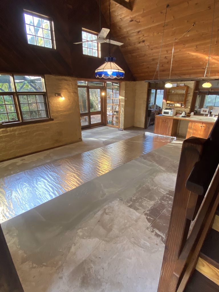 Living area of a stone cottage in Daylesford, Victoria, with reflective foil being rolled out over the existing concrete floor before the HOYA Ondol panels go down
