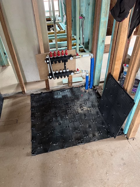 First HOYA Ondol panels laid over the particleboard subfloor beside the new manifold, in a timber-framed renovation in O'Connor, ACT
