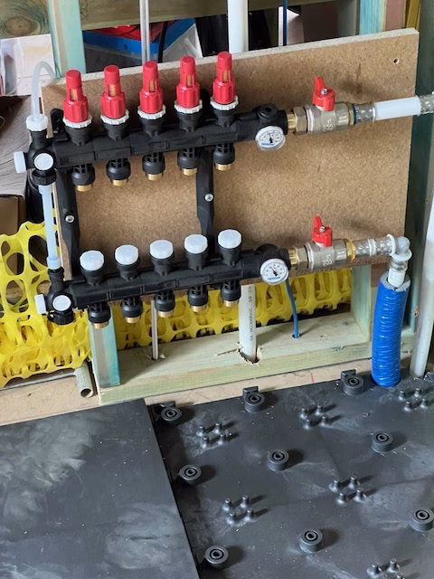 Hydronic floor heating manifold with flow and return valves mounted on a board above the HOYA Ondol panels