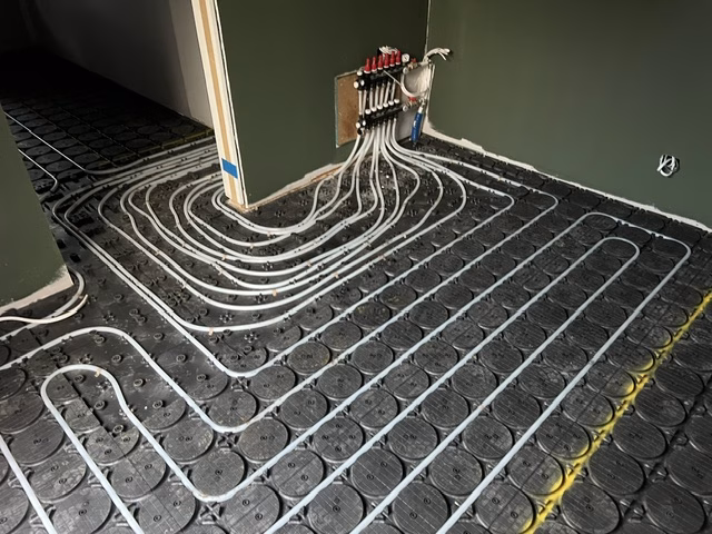 Hydronic pipe circuits running from a wall-mounted manifold across black HOYA Ondol panels into the surrounding rooms in the O'Connor ACT renovation