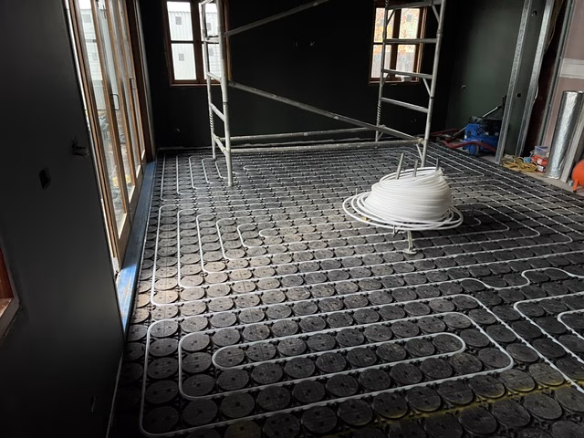 Large room in the O'Connor ACT renovation with white hydronic pipe loops laid in black HOYA Ondol panels and a coil of pipe on a dispenser