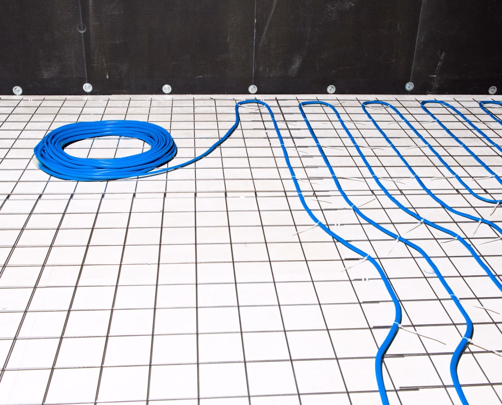 Blue electric heating cable laid out in loops over a grid before the concrete slab is poured, with a coil of cable still to be laid